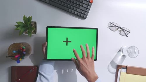 Top down view of man's hands using a mock up green screen tablet on white desk
