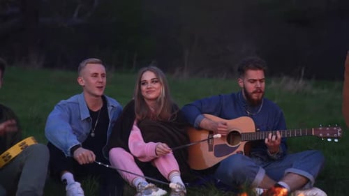 Friends Gathered Around Campfire Playing Music at Night