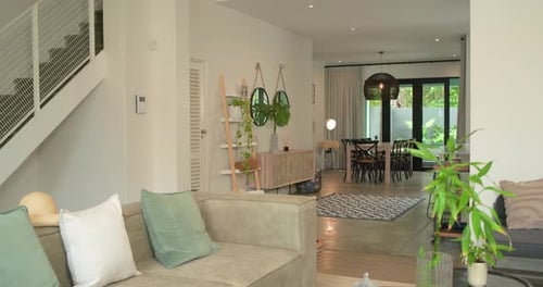 Camera is starting slow pan to right, revealing beige sectional sofa and dining area for staging