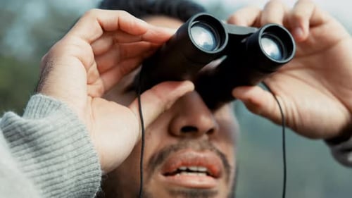 Face, hiking and binoculars with a man in nature for sightseeing or to explore a mountain