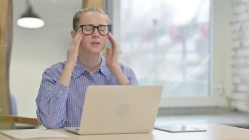 Stressed Woman Massaging Temples While Working on Laptop