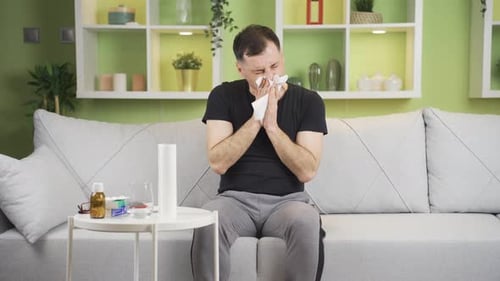 Man with Cold Blows Nose on Couch