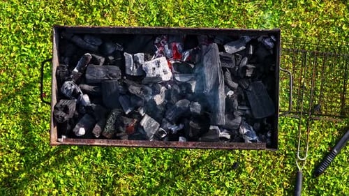 Top shot of barbeque grill with dark burning charcoal pieces at a field.