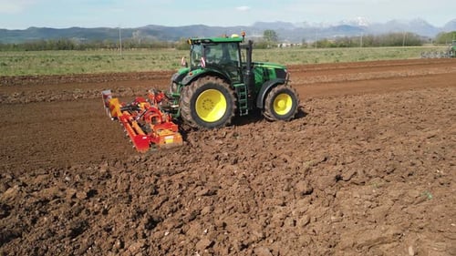 A Farmer is Seen Using a Cultivator to Till the Soil in a Large Agricultural Field The Dirt and Dust