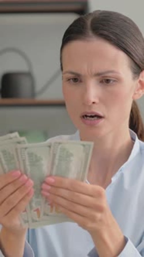 Portrait of Upset Young Woman Counting Money at Home