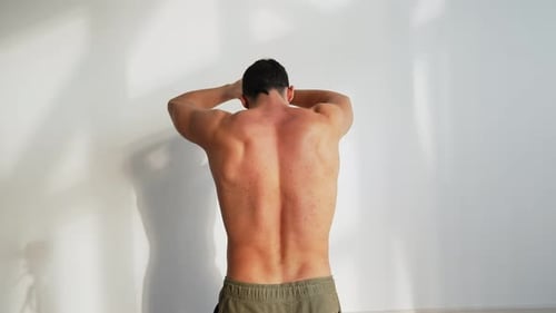 Man Stretching Shoulders Against White Wall Indoors