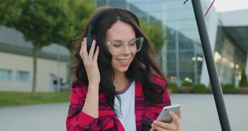 Close up portrait of smiling woman in glasses dressed which listening music in headphones from phone