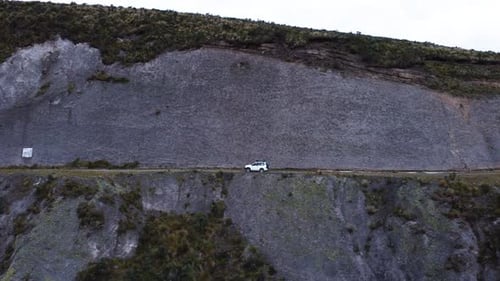 A dramatic aerial left pan shot following a car driving along a steep cliffside road in the Ecuadori
