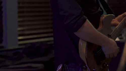 A Mans strumming a guitar very fast while performing with a band in a low lit venue in 4K