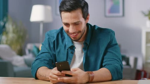 Smiling Young Man Using Smartphone at Table Indoors