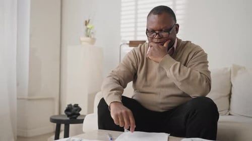 Worried Man Counting Money at Home on Sofa
