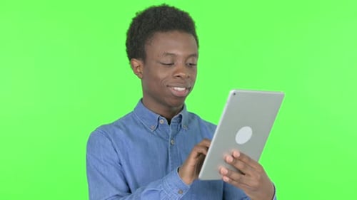 Young African Man using Digital Tablet on Green Background