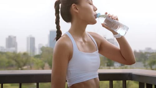 Young fitness woman in sportswear drinking water in city park