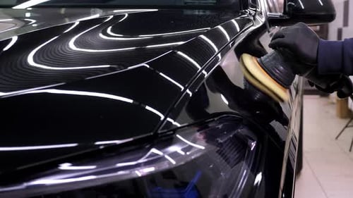 A Man Polishes a Black Car with a Car Polishing Machine at a Car Dealership