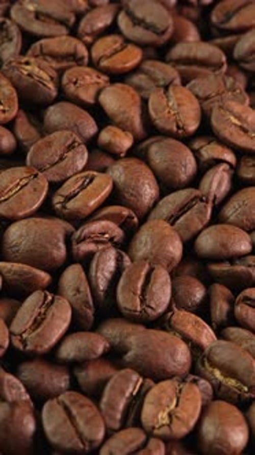 Vertical video roasted coffee beans rotating as background close-up macro top view