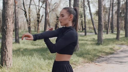 Young Woman Engaging in Arm Stretches Amidst Park's Natural Beauty