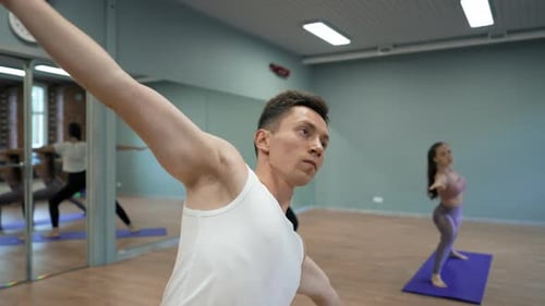 Young Coach Teaches Ladies to Stand in Yoga Pose Warrior