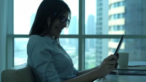 Cheerful businesswoman enjoys movie on tablet during break in city office