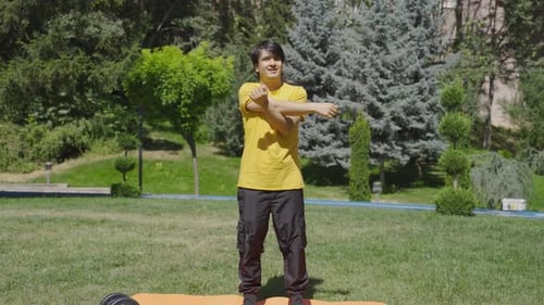 Young Adult Stretches Arm in Sunny Green Park
