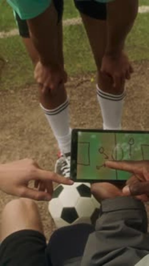 Vertical of Coach Reviewing Game Plan on Tablet with Youth Soccer Team