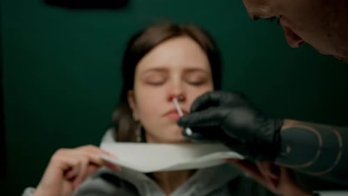 Interior de un estudio de piercings: el maestro de piercings hace un piercing para una niña, piercing para el tabique nasal