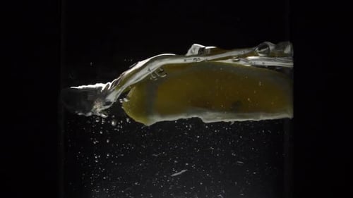 Slow Motion Of A Lemon Slice Falling Into A Glass Of Water Isolated In Black Background - medium sho