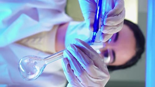 Scientist Pours Blue Liquid Into Round Bottom Flask