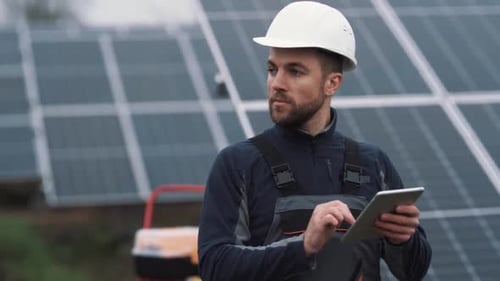 Porträt eines Arbeiters in einem Helm mit einem Tablet auf dem Hintergrund eines Solarkraftwerks