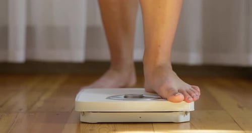 A Woman Measures Her Weight on White Scale on Floor Measuring Tape Falls Off