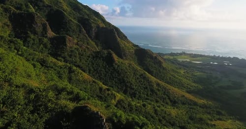 Sunlight falls over lush green mountains beside the shimmering ocean