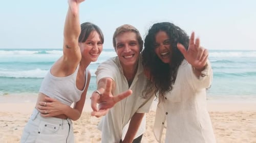 Young Diverse Friends Laugh Out Loud and Show Thumbs Up Stand on Sandy Beach
