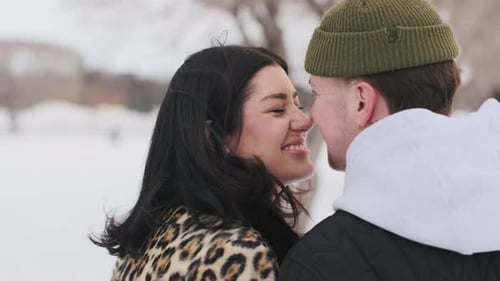 Happy young beautiful couple spend time in sunny winter forest together touching noses