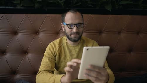 Young man browsing the internet on his tablet computer in a trendy cafe