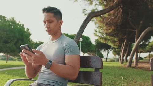 Young man sitting on a park bench uses a mobile phone