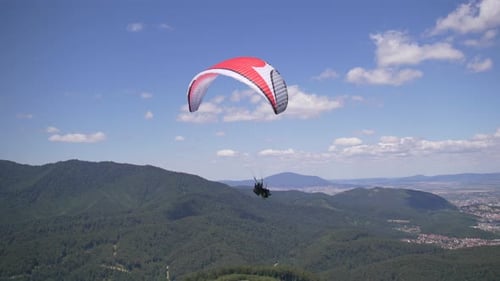 Fallschirmspringer, der im klaren blauen Himmel über der grünen Berglandschaft schwebt