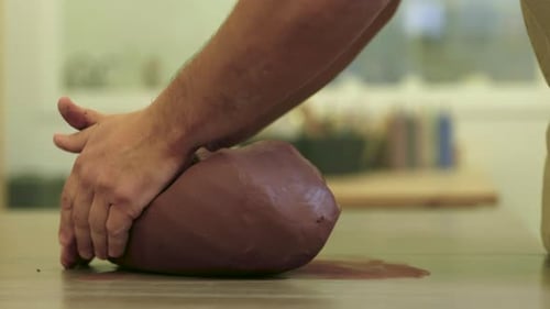 Male hands placing raw clay material onto studio work table preparing top sculpt block