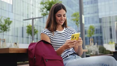 Happy Hispanic Student Girl Using Yellow Cell Phone Outdoors at University Campus Smiling Young