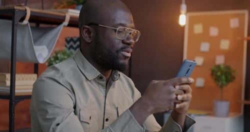 Man Smiling While Using Phone Indoors at Night