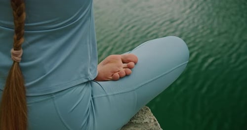 Meditating woman in a lotus pose beside a pristine lake, her braid draping down, symbolizing peace a