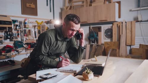 Carpenter Talking to a Furniture Customer on the Phone in His Own Workshop