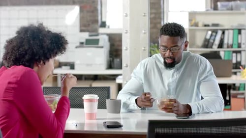 Diverse colleagues talking and having lunch at table in office in slow motion