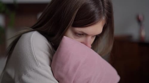 Gros plan, épuisée, jeune femme gelée, embrassant un oreiller rose, assise à la maison dans le salon triste
