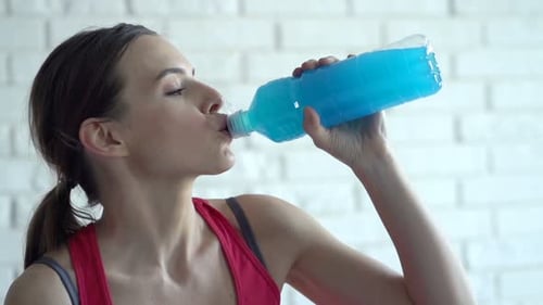 Woman drinking a blue energy drink indoors
