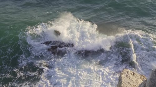 Tilting moving wide shot of powerful waves crushing in to rocks and an island in the horizon at the