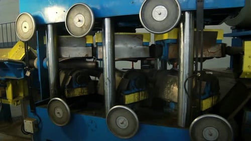 Machine rolls metal pole in industrial setting