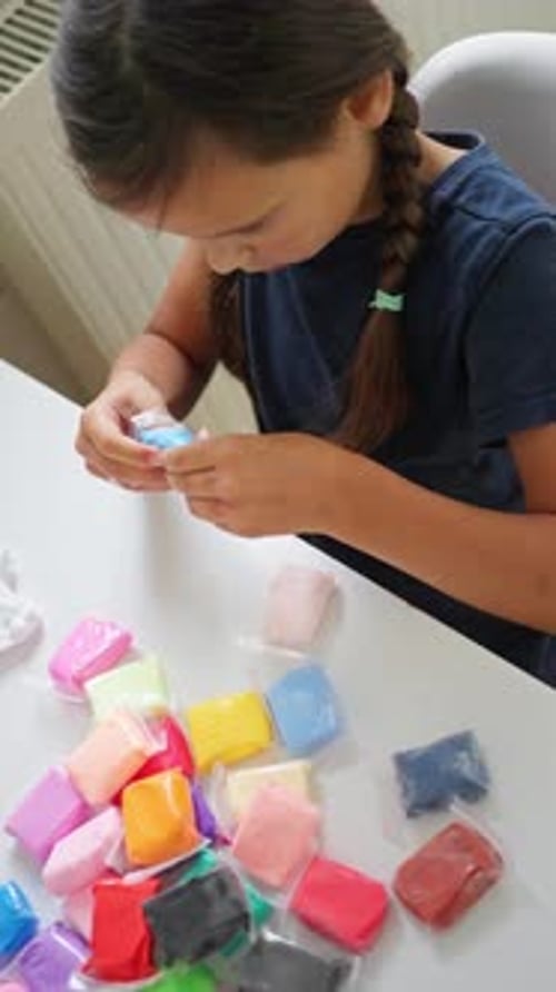 Niña blanca moldeando arcilla colorida en una mesa de cocina brillante, cabello trenzado con las manos para dar forma a las manos, azul pequeño