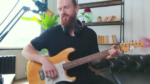 Blond Man Plays Guitar and Sings into Microphone