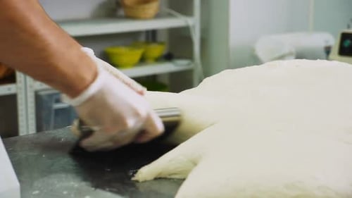 Hands Cutting Dough With Knife in Bright Workplace