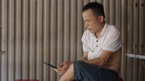Mature Asian Man Manipulates the Screen of His Smartphone Calm and Relaxed While Resting and Smiling
