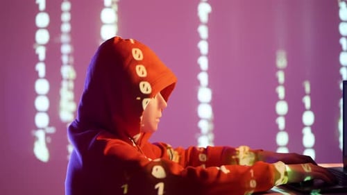 Anonymous Hacker in Orange Hoodie and Mask with Binary Code Projection on Face Turning Toward Camera